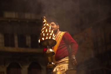 Varanasi, Uttar Pradesh, Hindistan - 20 Ocak 2024: Ganga aarti, Dashashwamedh ghat geleneksel elbise ve Hindu ayinleri ile kutsal nehir keneviri akşam ayini yapan genç bir rahibin portresi.