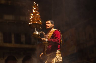 Varanasi, Uttar Pradesh, Hindistan - 20 Ocak 2024: Ganga aarti, Dashashwamedh ghat geleneksel elbise ve Hindu ayinleri ile kutsal nehir keneviri akşam ayini yapan genç bir rahibin portresi.