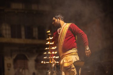 Varanasi, Uttar Pradesh, Hindistan - 20 Ocak 2024: Ganga aarti, Dashashwamedh ghat geleneksel elbise ve Hindu ayinleri ile kutsal nehir keneviri akşam ayini yapan genç bir rahibin portresi.