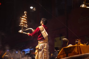 Varanasi, Uttar Pradesh, Hindistan - 20 Ocak 2024: Ganga aarti, Dashashwamedh ghat geleneksel elbise ve Hindu ayinleri ile kutsal nehir keneviri akşam ayini yapan genç bir rahibin portresi.