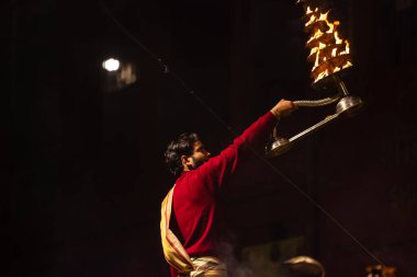 Varanasi, Uttar Pradesh, Hindistan - 20 Ocak 2024: Ganga aarti, Dashashwamedh ghat geleneksel elbise ve Hindu ayinleri ile kutsal nehir keneviri akşam ayini yapan genç bir rahibin portresi.