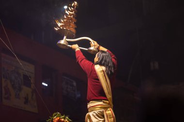 Varanasi, Uttar Pradesh, Hindistan - 20 Ocak 2024: Ganga aarti, Dashashwamedh ghat geleneksel elbise ve Hindu ayinleri ile kutsal nehir keneviri akşam ayini yapan genç bir rahibin portresi.