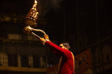 Varanasi, Uttar Pradesh, Hindistan - 20 Ocak 2024: Ganga aarti, Dashashwamedh ghat geleneksel elbise ve Hindu ayinleri ile kutsal nehir keneviri akşam ayini yapan genç bir rahibin portresi.