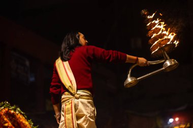 Varanasi, Uttar Pradesh, Hindistan - 20 Ocak 2024: Ganga aarti, Dashashwamedh ghat geleneksel elbise ve Hindu ayinleri ile kutsal nehir keneviri akşam ayini yapan genç bir rahibin portresi.