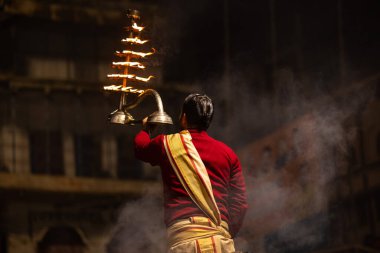 Varanasi, Uttar Pradesh, Hindistan - 20 Ocak 2024: Ganga aarti, Dashashwamedh ghat geleneksel elbise ve Hindu ayinleri ile kutsal nehir keneviri akşam ayini yapan genç bir rahibin portresi.