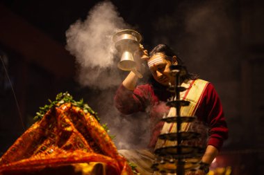 Varanasi, Uttar Pradesh, Hindistan - 20 Ocak 2024: Ganga aarti, Dashashwamedh ghat geleneksel elbise ve Hindu ayinleri ile kutsal nehir keneviri akşam ayini yapan genç bir rahibin portresi.