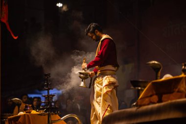 Varanasi, Uttar Pradesh, Hindistan - 20 Ocak 2024: Ganga aarti, Dashashwamedh ghat geleneksel elbise ve Hindu ayinleri ile kutsal nehir keneviri akşam ayini yapan genç bir rahibin portresi.