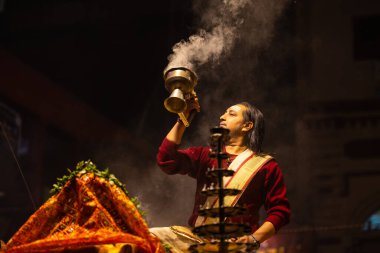 Varanasi, Uttar Pradesh, Hindistan - 20 Ocak 2024: Ganga aarti, Dashashwamedh ghat geleneksel elbise ve Hindu ayinleri ile kutsal nehir keneviri akşam ayini yapan genç bir rahibin portresi.