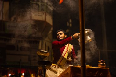 Varanasi, Uttar Pradesh, Hindistan - 20 Ocak 2024: Ganga aarti, Dashashwamedh ghat geleneksel elbise ve Hindu ayinleri ile kutsal nehir keneviri akşam ayini yapan genç bir rahibin portresi.