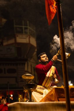 Varanasi, Uttar Pradesh, Hindistan - 20 Ocak 2024: Ganga aarti, Dashashwamedh ghat geleneksel elbise ve Hindu ayinleri ile kutsal nehir keneviri akşam ayini yapan genç bir rahibin portresi.