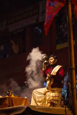 Varanasi, Uttar Pradesh, Hindistan - 20 Ocak 2024: Ganga aarti, Dashashwamedh ghat geleneksel elbise ve Hindu ayinleri ile kutsal nehir keneviri akşam ayini yapan genç bir rahibin portresi.