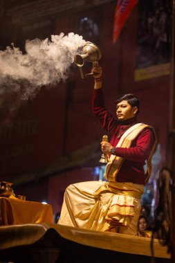 Varanasi, Uttar Pradesh, Hindistan - 20 Ocak 2024: Ganga aarti, Dashashwamedh ghat geleneksel elbise ve Hindu ayinleri ile kutsal nehir keneviri akşam ayini yapan genç bir rahibin portresi.