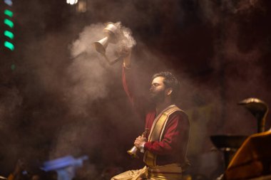 Varanasi, Uttar Pradesh, Hindistan - 20 Ocak 2024: Ganga aarti, Dashashwamedh ghat geleneksel elbise ve Hindu ayinleri ile kutsal nehir keneviri akşam ayini yapan genç bir rahibin portresi.