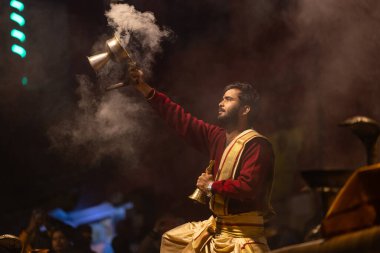 Varanasi, Uttar Pradesh, Hindistan - 20 Ocak 2024: Ganga aarti, Dashashwamedh ghat geleneksel elbise ve Hindu ayinleri ile kutsal nehir keneviri akşam ayini yapan genç bir rahibin portresi.