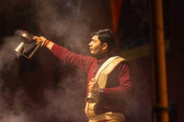 Varanasi, Uttar Pradesh, Hindistan - 20 Ocak 2024: Ganga aarti, Dashashwamedh ghat geleneksel elbise ve Hindu ayinleri ile kutsal nehir keneviri akşam ayini yapan genç bir rahibin portresi.