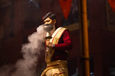 Varanasi, Uttar Pradesh, India - January 20 2024: Ganga aarti, Portrait of a young male priest performing holy river ganga evening aarti at dashashwamedh ghat in traditional dress with hindu rituals.