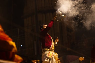 Varanasi, Uttar Pradesh, Hindistan - 20 Ocak 2024: Ganga aarti, Dashashwamedh ghat geleneksel elbise ve Hindu ayinleri ile kutsal nehir keneviri akşam ayini yapan genç bir rahibin portresi.