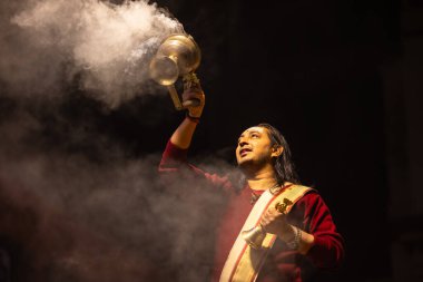 Varanasi, Uttar Pradesh, Hindistan - 20 Ocak 2024: Ganga aarti, Dashashwamedh ghat geleneksel elbise ve Hindu ayinleri ile kutsal nehir keneviri akşam ayini yapan genç bir rahibin portresi.