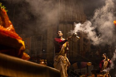 Varanasi, Uttar Pradesh, Hindistan - 20 Ocak 2024: Ganga aarti, Dashashwamedh ghat geleneksel elbise ve Hindu ayinleri ile kutsal nehir keneviri akşam ayini yapan genç bir rahibin portresi.
