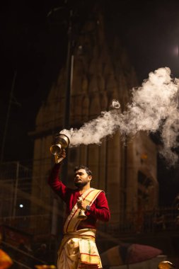 Varanasi, Uttar Pradesh, Hindistan - 20 Ocak 2024: Ganga aarti, Dashashwamedh ghat geleneksel elbise ve Hindu ayinleri ile kutsal nehir keneviri akşam ayini yapan genç bir rahibin portresi.