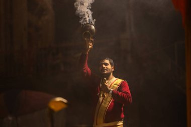 Varanasi, Uttar Pradesh, Hindistan - 20 Ocak 2024: Ganga aarti, Dashashwamedh ghat geleneksel elbise ve Hindu ayinleri ile kutsal nehir keneviri akşam ayini yapan genç bir rahibin portresi.