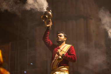 Varanasi, Uttar Pradesh, Hindistan - 20 Ocak 2024: Ganga aarti, Dashashwamedh ghat geleneksel elbise ve Hindu ayinleri ile kutsal nehir keneviri akşam ayini yapan genç bir rahibin portresi.