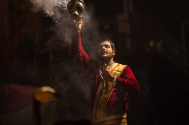 Varanasi, Uttar Pradesh, Hindistan - 20 Ocak 2024: Ganga aarti, Dashashwamedh ghat geleneksel elbise ve Hindu ayinleri ile kutsal nehir keneviri akşam ayini yapan genç bir rahibin portresi.