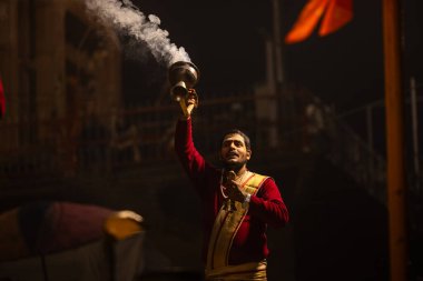 Varanasi, Uttar Pradesh, Hindistan - 20 Ocak 2024: Ganga aarti, Dashashwamedh ghat geleneksel elbise ve Hindu ayinleri ile kutsal nehir keneviri akşam ayini yapan genç bir rahibin portresi.