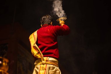 Varanasi, Uttar Pradesh, Hindistan - 20 Ocak 2024: Ganga aarti, Dashashwamedh ghat geleneksel elbise ve Hindu ayinleri ile kutsal nehir keneviri akşam ayini yapan genç bir rahibin portresi.