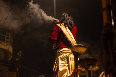 Varanasi, Uttar Pradesh, Hindistan - 20 Ocak 2024: Ganga aarti, Dashashwamedh ghat geleneksel elbise ve Hindu ayinleri ile kutsal nehir keneviri akşam ayini yapan genç bir rahibin portresi.
