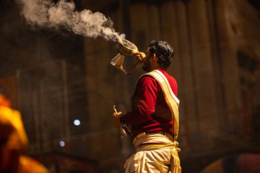 Varanasi, Uttar Pradesh, Hindistan - 20 Ocak 2024: Ganga aarti, Dashashwamedh ghat geleneksel elbise ve Hindu ayinleri ile kutsal nehir keneviri akşam ayini yapan genç bir rahibin portresi.