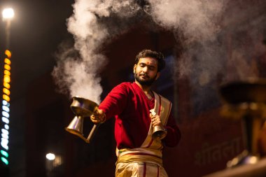Varanasi, Uttar Pradesh, Hindistan - 20 Ocak 2024: Ganga aarti, Dashashwamedh ghat geleneksel elbise ve Hindu ayinleri ile kutsal nehir keneviri akşam ayini yapan genç bir rahibin portresi.