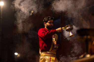 Varanasi, Uttar Pradesh, Hindistan - 20 Ocak 2024: Ganga aarti, Dashashwamedh ghat geleneksel elbise ve Hindu ayinleri ile kutsal nehir keneviri akşam ayini yapan genç bir rahibin portresi.