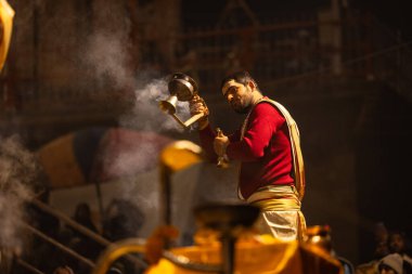Varanasi, Uttar Pradesh, Hindistan - 20 Ocak 2024: Ganga aarti, Dashashwamedh ghat geleneksel elbise ve Hindu ayinleri ile kutsal nehir keneviri akşam ayini yapan genç bir rahibin portresi.