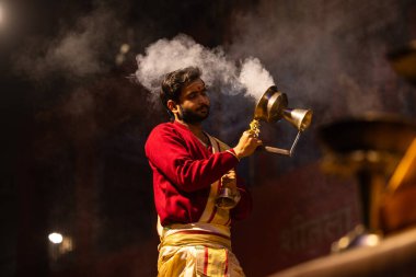 Varanasi, Uttar Pradesh, Hindistan - 20 Ocak 2024: Ganga aarti, Dashashwamedh ghat geleneksel elbise ve Hindu ayinleri ile kutsal nehir keneviri akşam ayini yapan genç bir rahibin portresi.