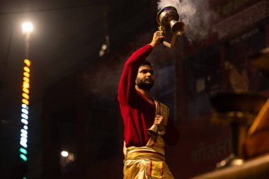 Varanasi, Uttar Pradesh, Hindistan - 20 Ocak 2024: Ganga aarti, Dashashwamedh ghat geleneksel elbise ve Hindu ayinleri ile kutsal nehir keneviri akşam ayini yapan genç bir rahibin portresi.