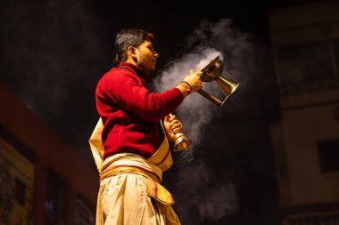 Varanasi, Uttar Pradesh, Hindistan - 20 Ocak 2024: Ganga aarti, Dashashwamedh ghat geleneksel elbise ve Hindu ayinleri ile kutsal nehir keneviri akşam ayini yapan genç bir rahibin portresi.