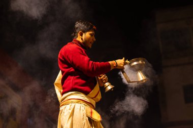 Varanasi, Uttar Pradesh, Hindistan - 20 Ocak 2024: Ganga aarti, Dashashwamedh ghat geleneksel elbise ve Hindu ayinleri ile kutsal nehir keneviri akşam ayini yapan genç bir rahibin portresi.