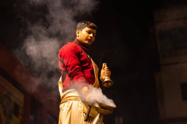 Varanasi, Uttar Pradesh, Hindistan - 20 Ocak 2024: Ganga aarti, Dashashwamedh ghat geleneksel elbise ve Hindu ayinleri ile kutsal nehir keneviri akşam ayini yapan genç bir rahibin portresi.