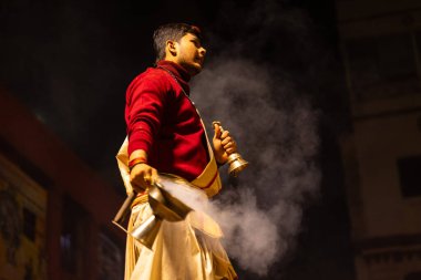 Varanasi, Uttar Pradesh, Hindistan - 20 Ocak 2024: Ganga aarti, Dashashwamedh ghat geleneksel elbise ve Hindu ayinleri ile kutsal nehir keneviri akşam ayini yapan genç bir rahibin portresi.