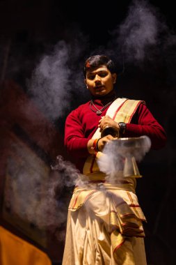 Varanasi, Uttar Pradesh, Hindistan - 20 Ocak 2024: Ganga aarti, Dashashwamedh ghat geleneksel elbise ve Hindu ayinleri ile kutsal nehir keneviri akşam ayini yapan genç bir rahibin portresi.