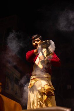 Varanasi, Uttar Pradesh, Hindistan - 20 Ocak 2024: Ganga aarti, Dashashwamedh ghat geleneksel elbise ve Hindu ayinleri ile kutsal nehir keneviri akşam ayini yapan genç bir rahibin portresi.