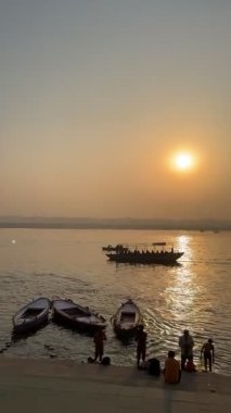 Varanasi, Uttar Pradesh, Hindistan - 12 Mart 2025: Varanasi 'de kış sabahı gündoğumunda nehir keneviri kıyısında yüzen veya parkedilmiş tahta botların sinematografik görüntüsü.