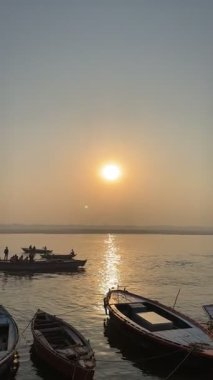 Varanasi, Uttar Pradesh, Hindistan - 12 Mart 2025: Varanasi 'de kış sabahı gündoğumunda nehir keneviri kıyısında yüzen veya parkedilmiş tahta botların sinematografik görüntüsü.