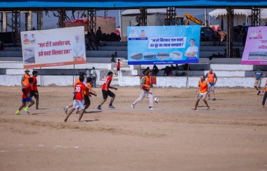 Çocuklar kumlu zeminde futbol oynuyor.
