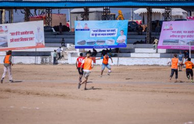 Çocuklar kumlu zeminde futbol oynuyor.