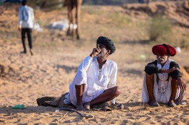 Puşkar, Rajasthan, Hindistan - Kasım 09 2024: Geleneksel beyaz giysili rajasthani erkek portresi çöl panayırında deve fuarı sırasında deve ticareti sırasında sarıklı.