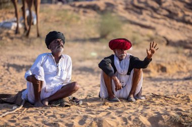 Puşkar, Rajasthan, Hindistan - Kasım 09 2024: Geleneksel beyaz giysili rajasthani erkek portresi çöl panayırında deve fuarı sırasında deve ticareti sırasında sarıklı.