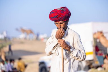 Puşkar, Rajasthan, Hindistan - Kasım 09 2024: Geleneksel beyaz giysili rajasthani erkek portresi çöl panayırında deve fuarı sırasında deve ticareti sırasında sarıklı.