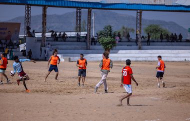 Çocuklar kumlu zeminde futbol oynuyor.